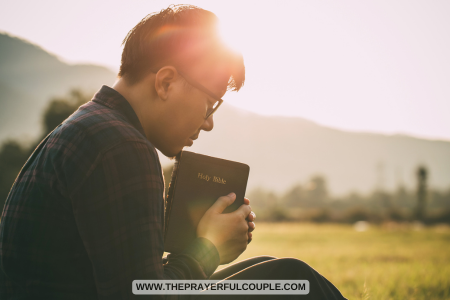 teen boy sitting in field and praying with Bible in hand