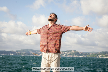 young man standing by ocean with arms outstretched