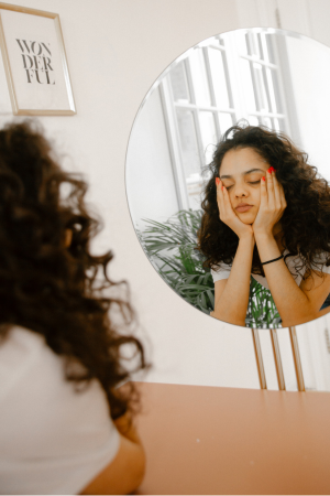 young woman looking into mirror sadly